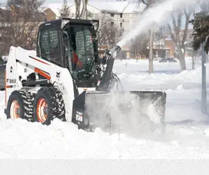 A Bobcat skid steer with a snowblower attachment throwing snow